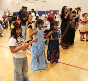 Children in colorful costumes dancing together on a wooden floor.