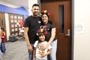 Couple posing for a picture in front of a classroom door, with a child standing behind them.
