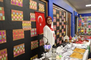 Woman standing in front of a bulletin board covered with colorful post-it notes, flags, and food items.