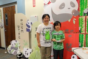 Woman and child standing in front of a colorful display featuring panda decorations.