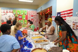 People gathered at a buffet table in a room decorated for an event, with food and party supplies visible.