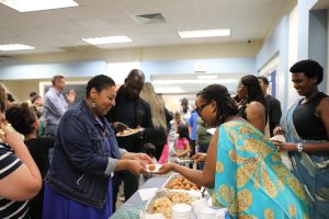 People gathered in a room, enjoying food at a buffet table.