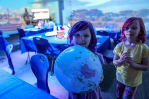 Two young girls holding a globe in a room with tables and chairs.