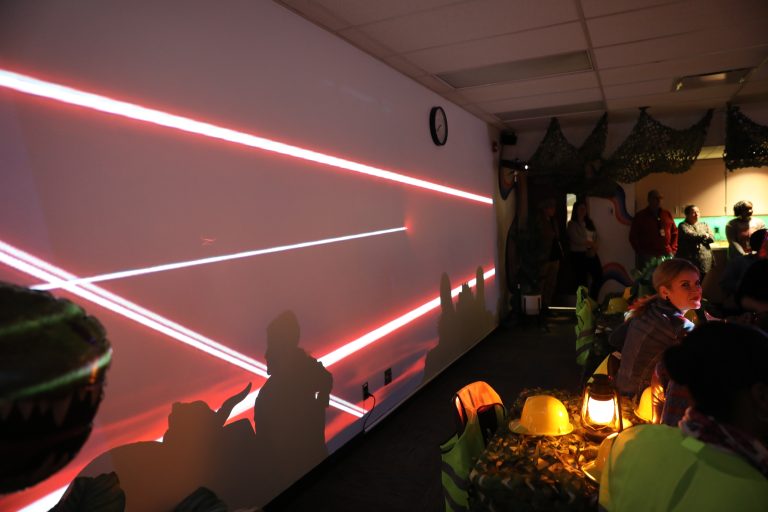People in a room with red laser beams on the wall.