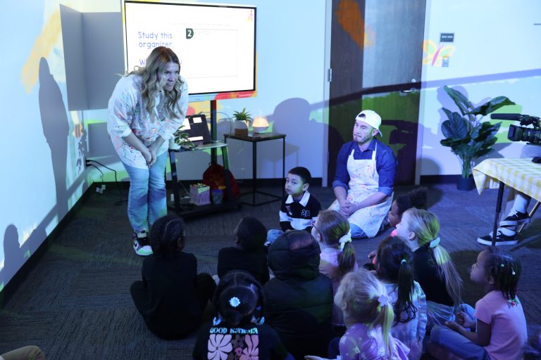 Woman standing in front of children, giving a presentation.