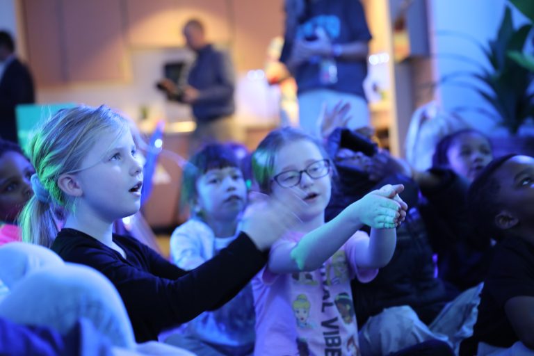 Children sitting in a dark room watching something on a screen.