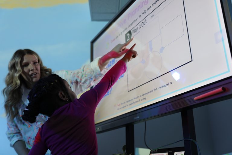 Woman teaching child how to use a whiteboard.