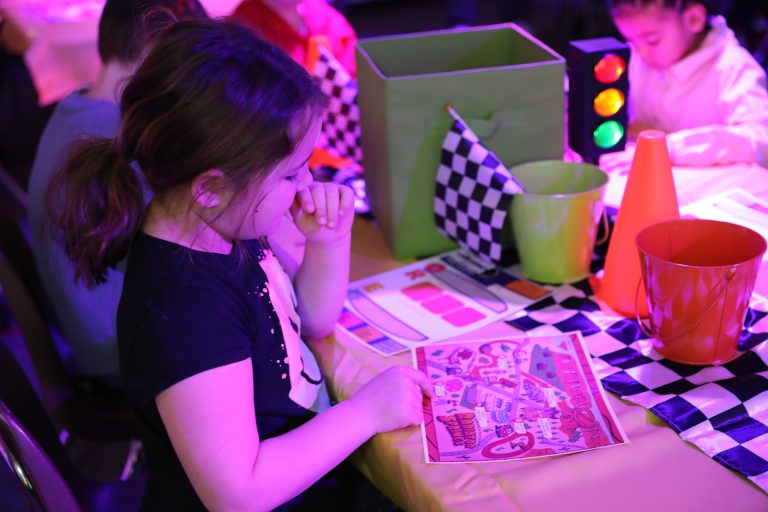 Little girl sitting at a table with colorful items in front of her.