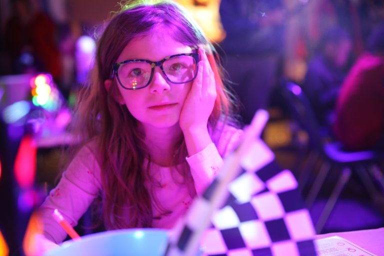 Young girl in glasses sitting at a table with a checkered tablecloth.