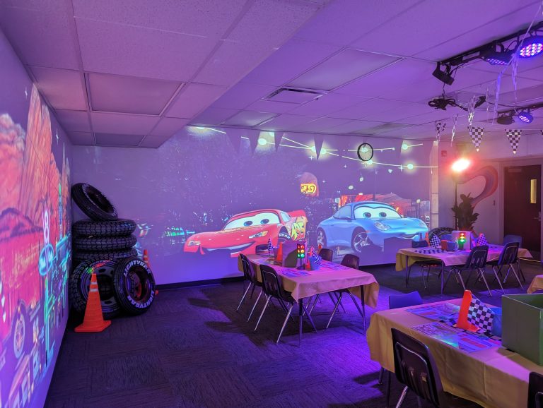 A vibrant children's party room with a Cars-themed projection on the wall and a table set up for guests.
