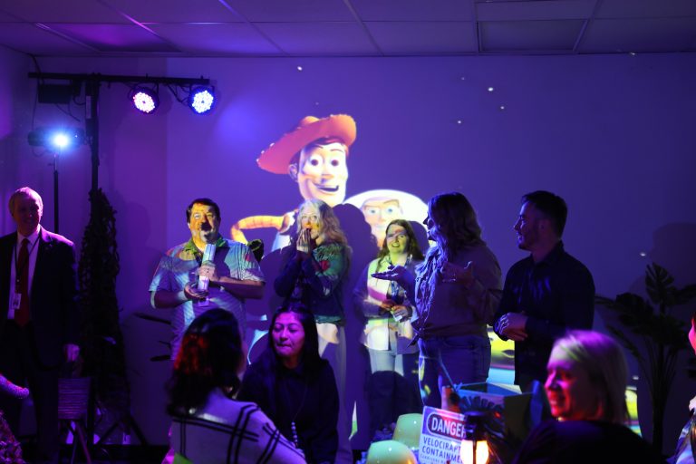 Group of people gathered in a room with a large projection screen displaying an image of animated characters.