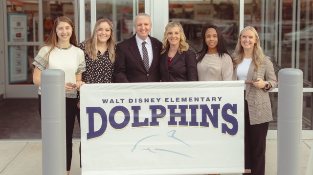 Walt Disney staff and PHM Superintendent holding Walt Disney sign