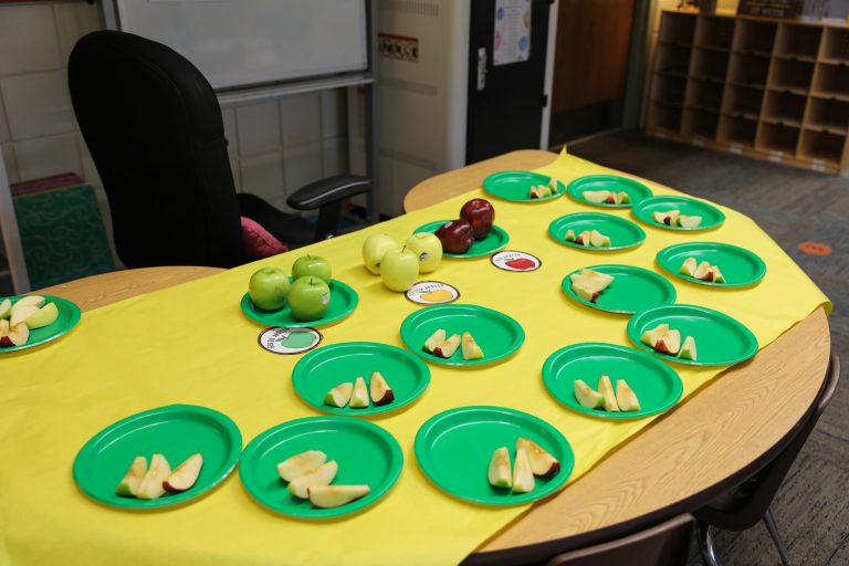 Table set up for a classroom party with plates of fruit and disposable tableware.