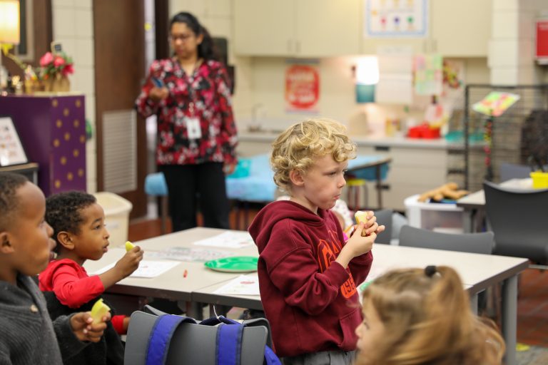Children eating snacks at a table in a classroom setting.