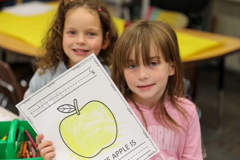 Two children holding up a drawing of an apple at school.