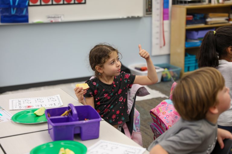 Girl in classroom giving thumbs up to camera.