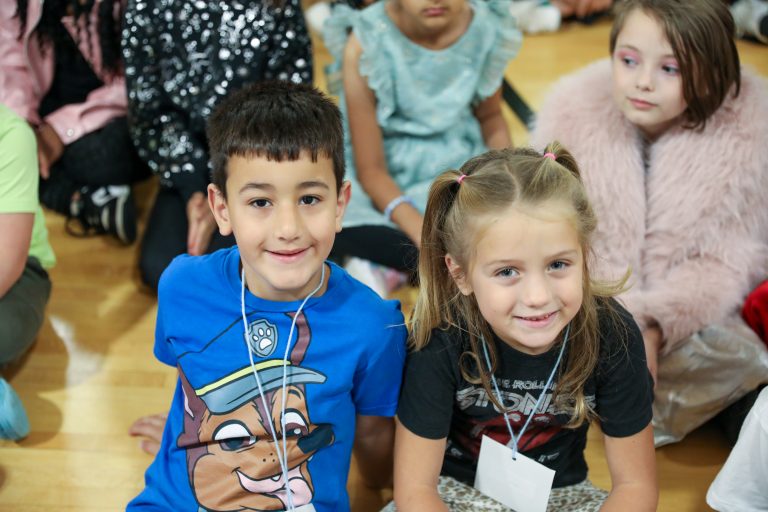 Two children sitting on floor in front of group of people.