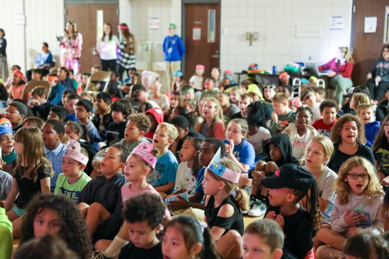Children sitting in a large auditorium, watching a performance.