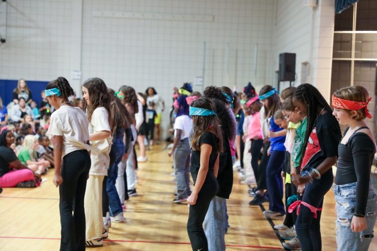 Group of people in a gymnasium, all wearing bandanas, standing in a line and facing the same direction.