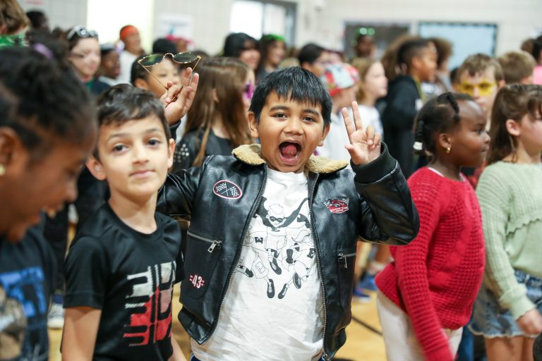 Children standing in a line, each waving at the camera.