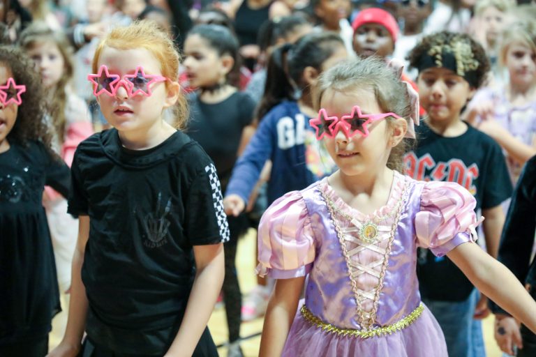 Children in colorful costumes dancing together on stage.