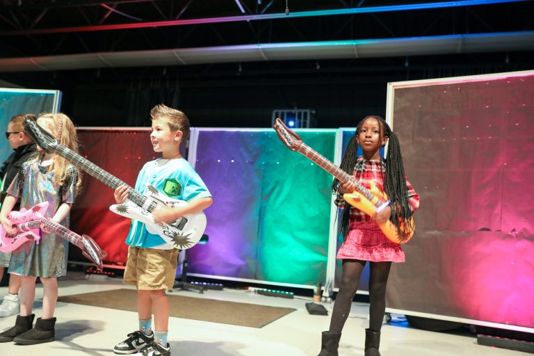 Three children holding guitars on stage.