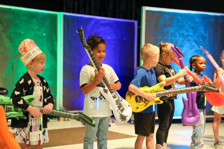 Children holding guitars on stage.