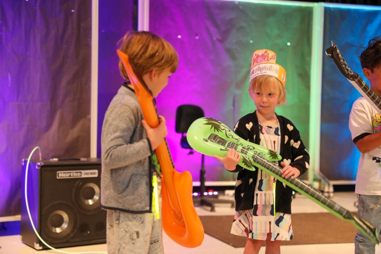 Two children holding toy instruments on stage.