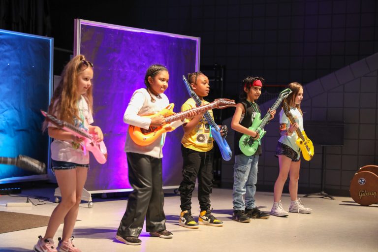 Five children playing guitars on stage.