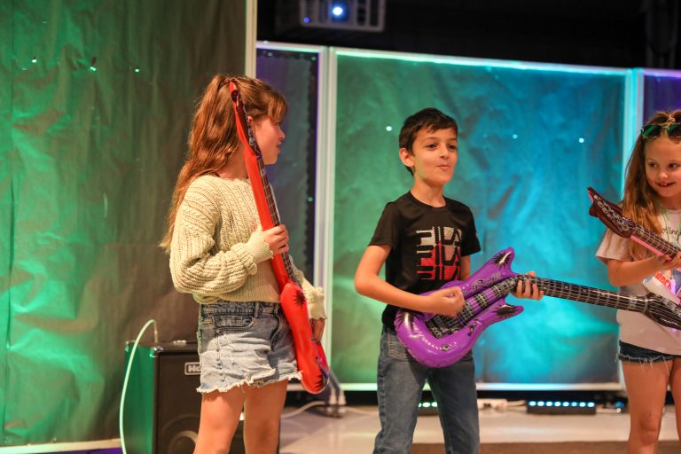 Three children playing guitars on stage.