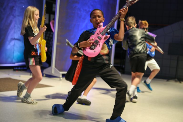 Children playing musical instruments on stage.