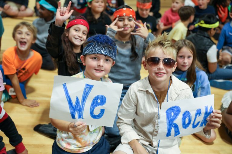 Children holding signs that say "we rock" in a gymnasium.