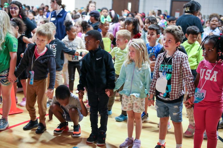 Children and adults standing in a group on a basketball court.