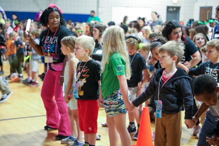 Children in a line at an event, possibly a school function or sports team gathering, waiting for their turn to participate