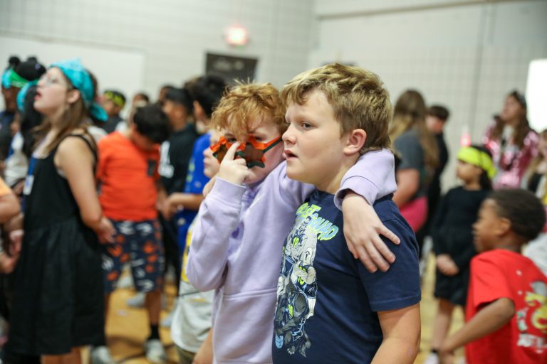 Two children hugging in a school gymnasium during a party.