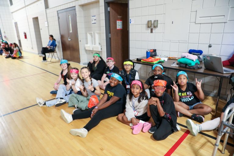 Group of people sitting on gym floor, posing for picture.
