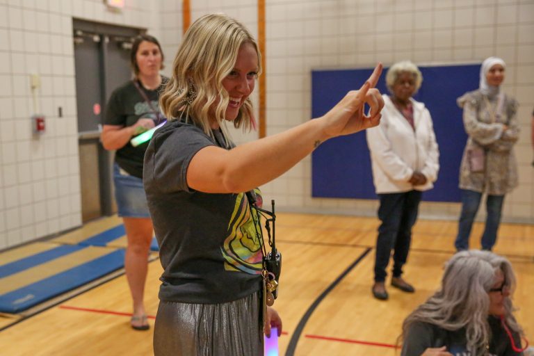 Woman in a gymnasium pointing at something with her right hand.