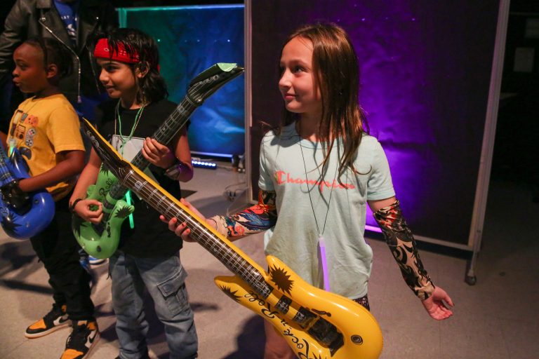 Three children holding guitars at a party.