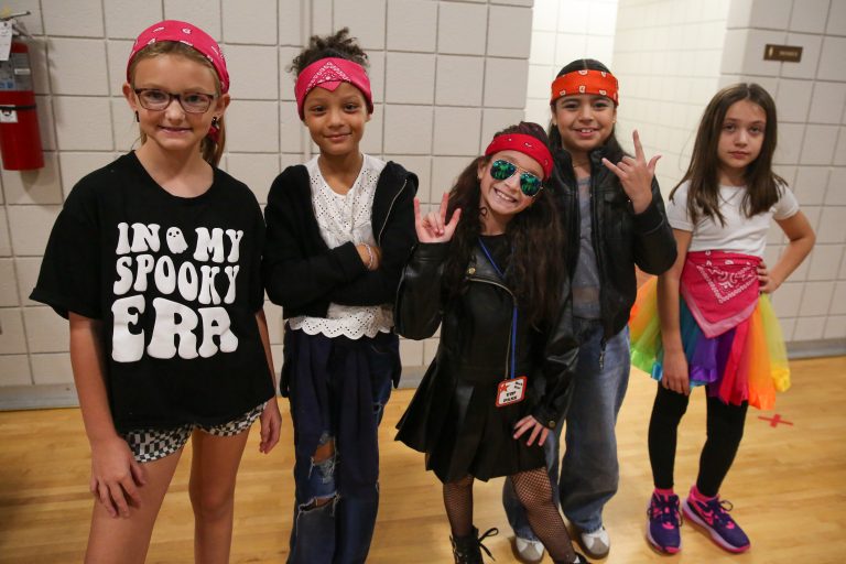 Five children posing in a gymnasium, all wearing bandanas, sunglasses and holding peace signs.