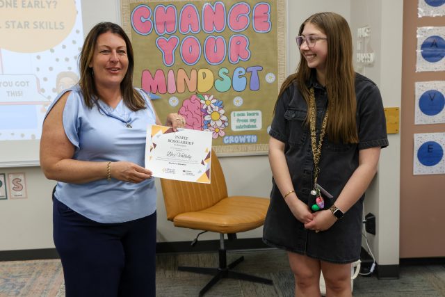Two people standing in front of a sign that says "change your mindset". One person is holding a certificate and smiling at