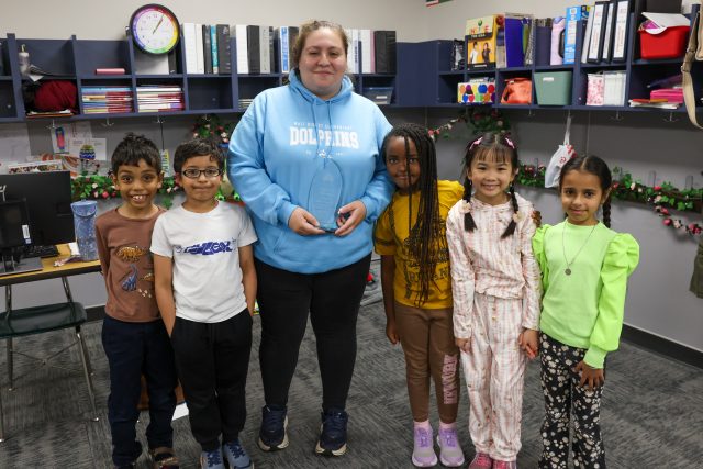 Woman standing in front of children, smiling at camera.