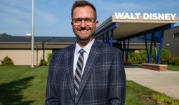 Man in suit standing in front of a sign that says "Walt Disney".