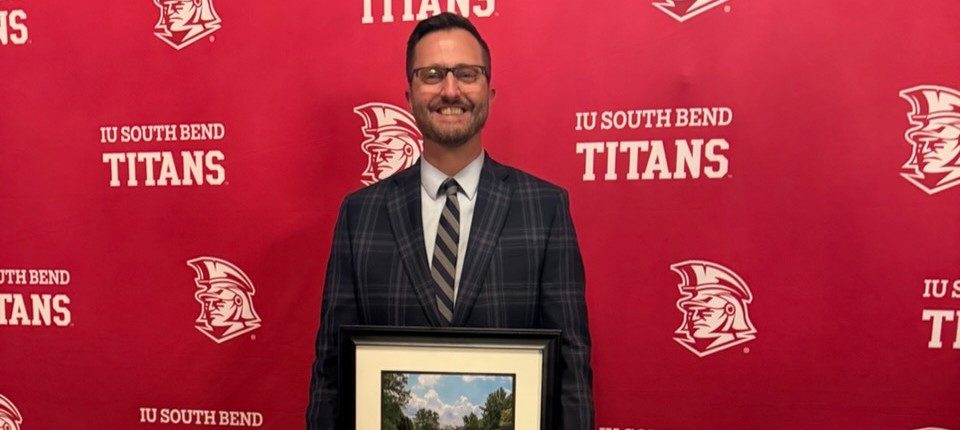 Mr. Matt Garber posing with his IUSB Alumni of the Year award standing in front of an IU South Bend Titans backdrop