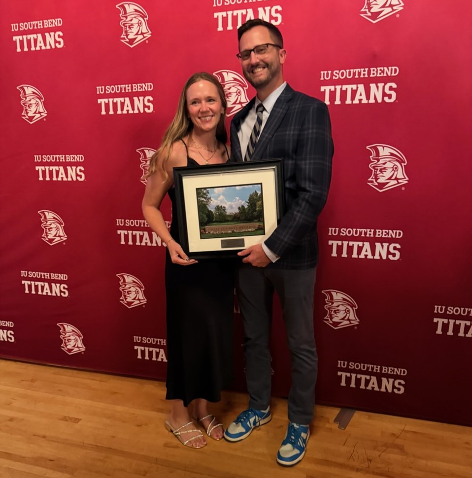 Mr. Matt Garber and his wife posing with his IUSB Alumni of the Year award standing in front of an IU South Bend Titans backdrop
