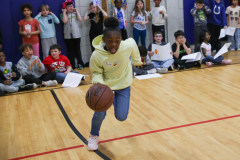 Young boy in yellow jacket dribbling basketball on court.