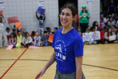 A woman in a blue shirt stands on a basketball court, smiling at the camera.