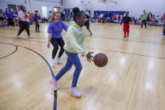 Girl in blue jeans dribbling a basketball on an indoor court.