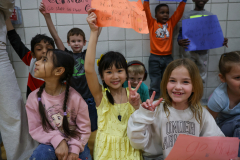 Children holding signs in a school gymnasium.