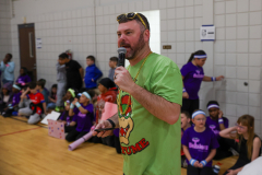 Man in green shirt holding microphone at podium, speaking to seated audience.